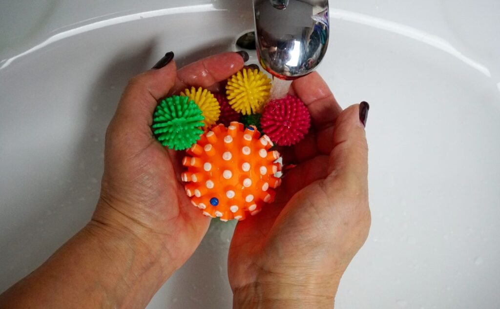 Hands rinsing colorful textured rubber balls under running water